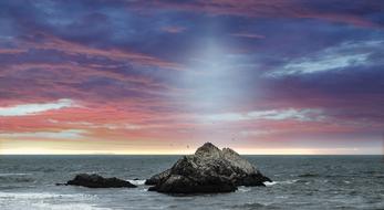 rock in the ocean against the background of a purple-blue sky