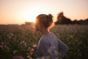 Blonde girl in glasses among the colorful and beautiful field with plants with flowers, at beautiful and colorful sunset