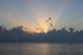 sun near horizon behind clouds at calm sea