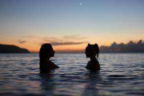 two Women bathing in lake at sunset