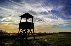 Silhouette of the tower, on the beautiful field with colorful plants, at colorful and beautiful sunset among the clouds