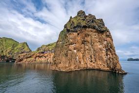 Beautiful and colorful rocks with green plants, among the water, under the blue sky with white clouds