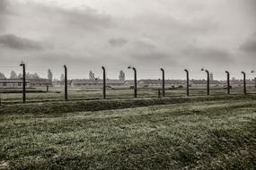 Fence of the Auschwitz 2 on the green grass, in Brezinka, Poland, under the clouds