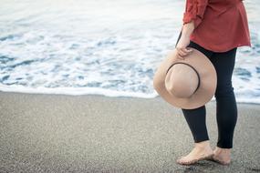 Woman with hat, walking on the sandy beach with waves