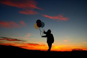 Silhouette of the girl with colorful balloons, on the beautiful landscape, at colorful and beautiful sunset with clouds