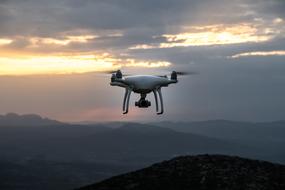 Close-up of the flying drone, above the beautiful mountains, under the colorful and beautiful dawn among the clouds