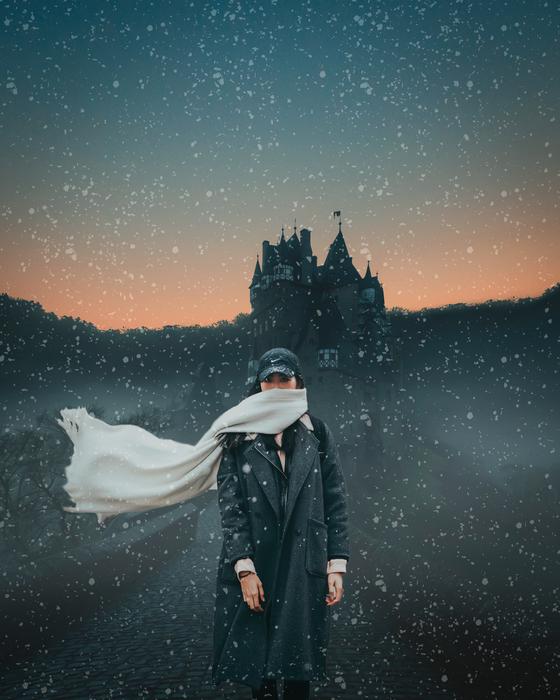 girl with a scarf in a blizzard stands against the background of the castle