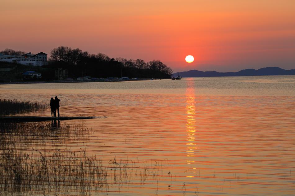 silhouettes of people on the shore of the lake on the background of sunset
