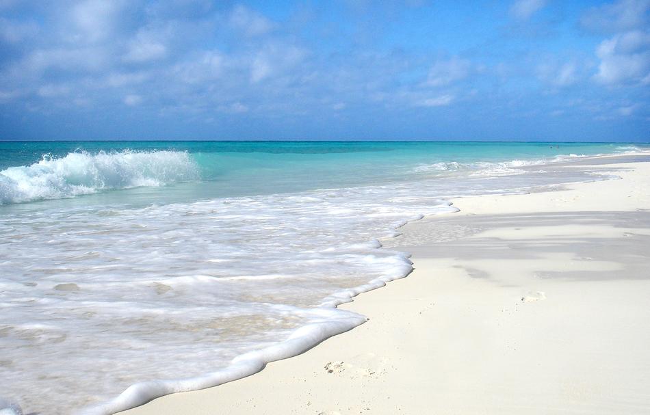 Beautiful sandy beach of Cuba, with colorful water with waves, under the blue sky with clouds