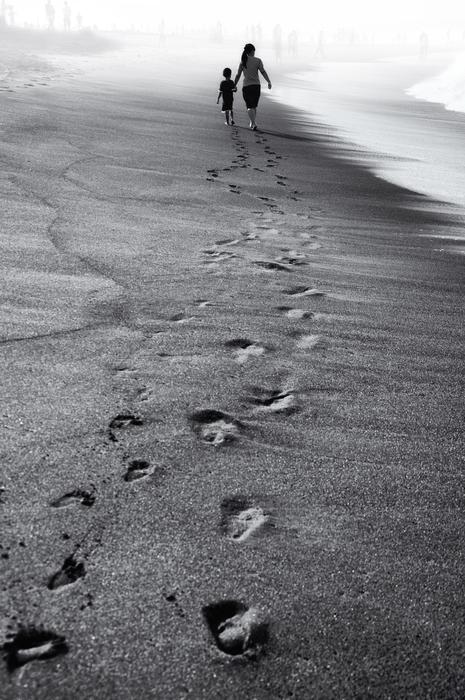 Black and white photo of the sandy beach with walking people, with footprints