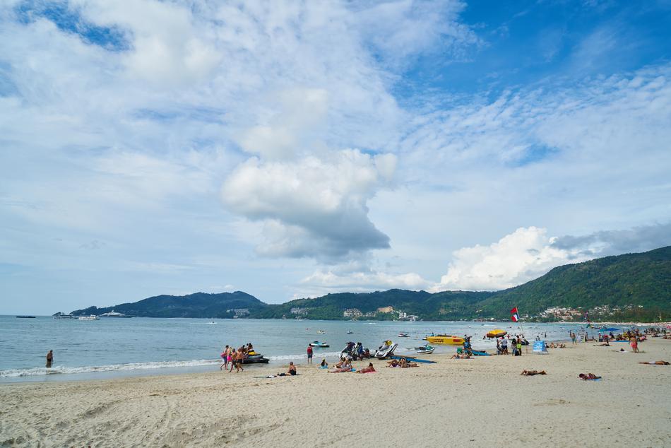 Beautiful landscape of the sandy beach with people, near the mountains with green plants, in Thailand