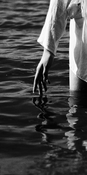 Black and white photo with close-up of the hand of a girl, walking in the water with ripple