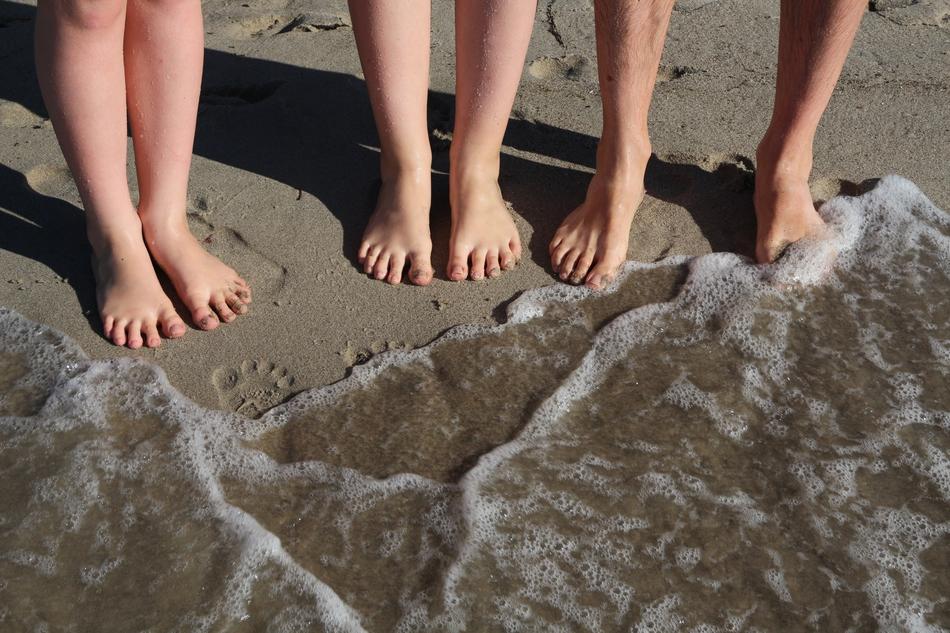 People standing barefoot, on the sandy beach of the sea with waves
