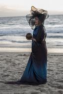 woman in dress and hat holding globe in hand on the beach