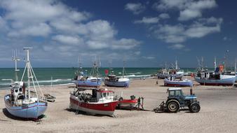 Colorful fishing boats and vehicles on the sandy beach with waves, under the blue sky with clouds