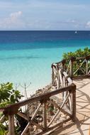 Beautiful, sandy Caribbean beach with green plants and wooden fence, in sunlight