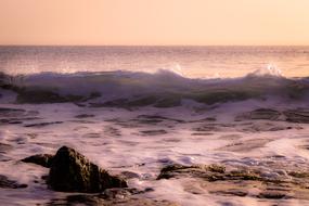 Beautiful beach with rocks, in waves, at colorful and beautiful sunset