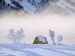 snow on the roof of the hut at the foot of the hill