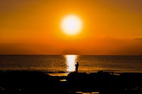 Silhouette of the fisherman on the beautiful rocky coast of Ayia Napa, Cyprus, Greece, at beautiful and colorful sunset