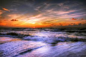 Beautiful and colorful beach of the North Sea in Denmark, with waves, at colorful and beautiful sunset among the clouds
