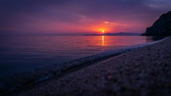 Beautiful landscape of the beach with waves, at colorful and beautiful dawn with clouds, behind the mountains