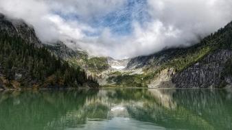 white clouds over a green lake in a mountain valley