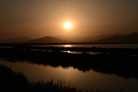 Beautiful landscape with silhouettes of the plants, among the water, near the mountains, at beautiful sunset