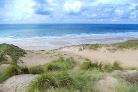 Beautiful Penhale Sands with green plants on the beach in Perranporth, Cornwall, England, under the sky with clouds