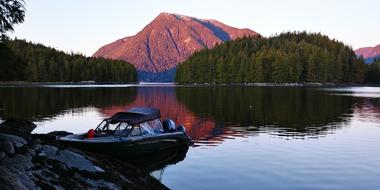 Beautiful landscape of the lake with boat, among the trees and mountains, at colorful and beautiful sunset