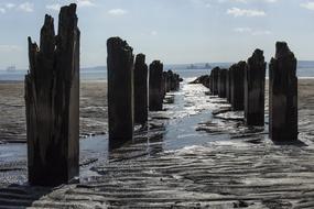 Beautiful, old pier in water, on the beach in sunlight, under the blue sky with clouds