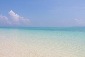 Landscape of the sandy beach if the sea, with turquoise water, in sunlight, under the blue sky with clouds