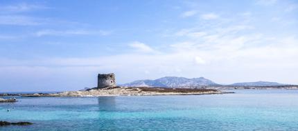 Beautiful landscape of the coast of Stintino, Sardinia, Italy, with the tower, among the turquoise water, under the blue sky with clouds