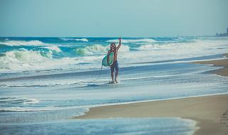 happy man with surfboard walks on beach