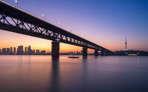 long bridge over calm water in view of city at dusk