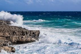 Beautiful, rocky shore of the sea, with colorful waves in sunlight, under the blue sky wih