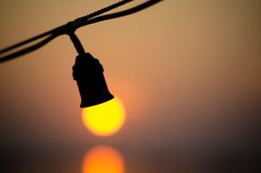 yellow light bulb on wire on blurred sunset background