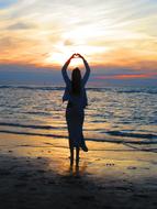 Silhouette of the girl, on the beautiful sandy beach with waves, at colorful and beautiful sunset with clouds