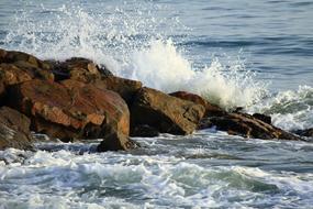 Close-up of the colorful rocks on the beautiful sea beach with waves, in sunlight
