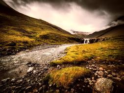 Beautiful and colorful landscape of the stream among the colorful mountains in Iceland, under the clouds