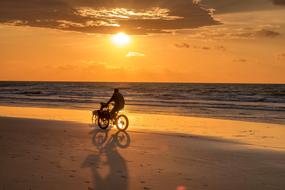 Person, riding on the bicycle, on the sandy beach, at colorful and beautiful sunset among the clouds