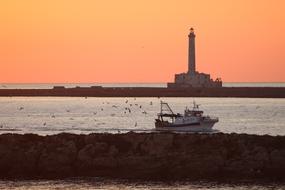 Fishing boat on sea near beach in view of lighthouse