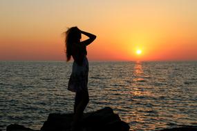 silhouette of a girl on a large stone on the coast at dusk