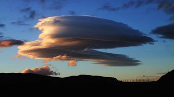 Lenticular cloud above the beautiful landscape with silhouettes, in Iceland, at colorful and beautiful sunset