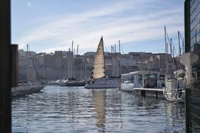 Beautiful landscape with boats on the water, among the buildings, under the blue sky with white clouds, in Marseille, France