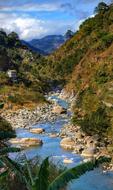 Beautiful and colorful landscape with the river, among the mountains with plants, under the blue sky with clouds