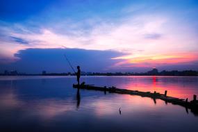 Person fishing on the bay of the lake in Vietnam, at colorful and beautiful sunset among the clouds