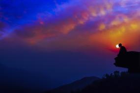 Silhouette of the person, meditating on the cliff, at colorful and beautiful dusk with clouds