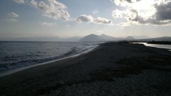Beautiful beach of Sardinia, Italy, with mountains, under the sky with clouds in sunlight