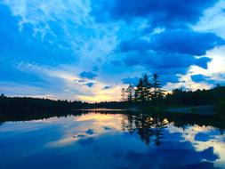 Beautiful lake with reflections, among the trees, at colorful and beautiful sunset with clouds