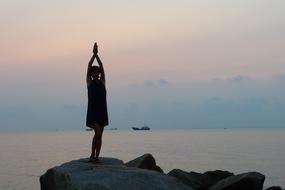 girl with raised hands on a stone on the coast